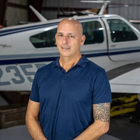 A man in a blue shirt is standing in front of a small plane.
