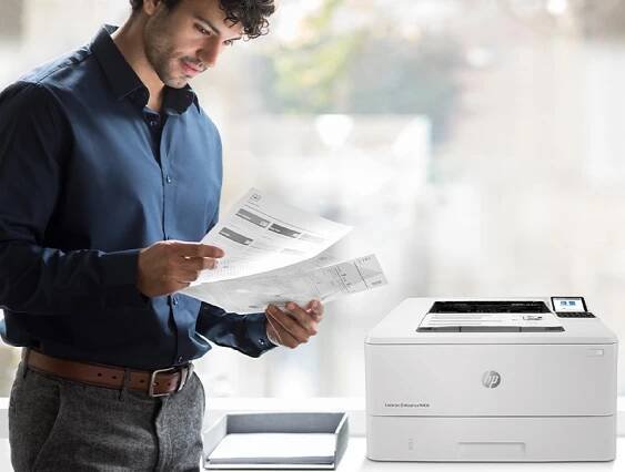 Muž stojí u multifunkční tiskárny HP LaserJet Enterprise a prohlíží si vytištěné dokumenty
