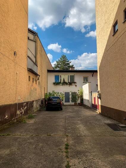Free An urban alleyway scene featuring a parked car and a residential building under a blue sky. Stock Photo