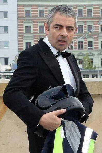a man in a tuxedo holding a helmet and jacket