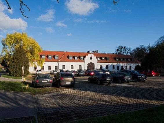 Vpredu parkovisko, vzadu biela budova s červenou strechou.