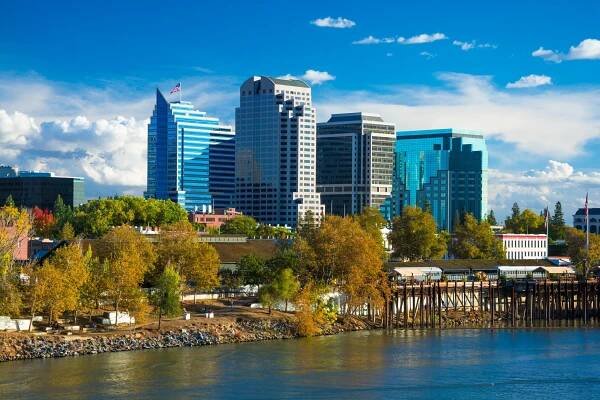 Sacramento downtown skyline during Autumn with Autumn colored trees in the foreground, with the Sacramento River, and dramatic clouds in the background.