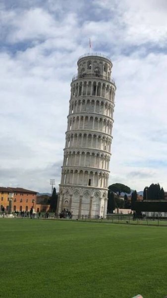 the leaning tower of pisa in italy is seen from across the grass, with people walking around