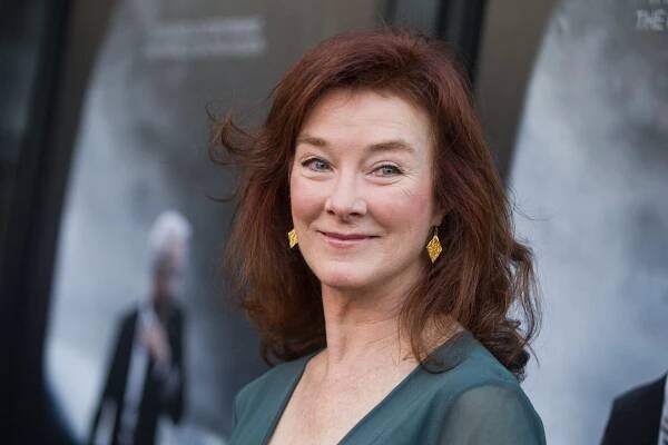 The actress Valerie Mahaffey, wearing a green top and golden earrings, smiles. She has reddish hair and green eyes.