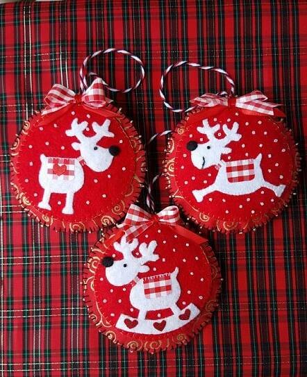 three red ornaments with white reindeers on them sitting on a plaid tablecloth background
