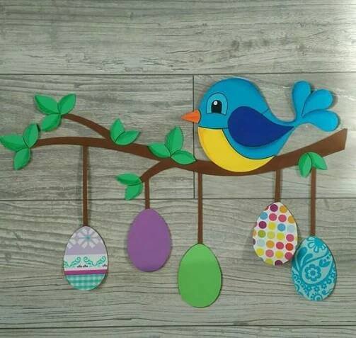 a blue bird sitting on top of a tree branch with painted eggs hanging from it