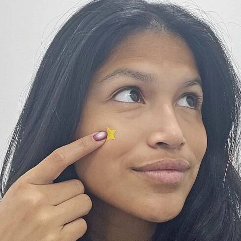 Woman applies a yellow star-shaped pimple patch to her cheek.