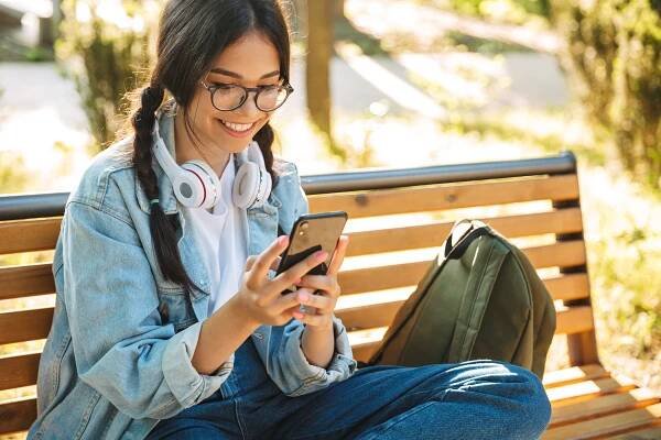 Smiling student using a smartphone on a park bench.