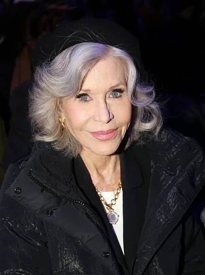 Person in a stylish coat and beret, with wavy hair, smiling at a public event