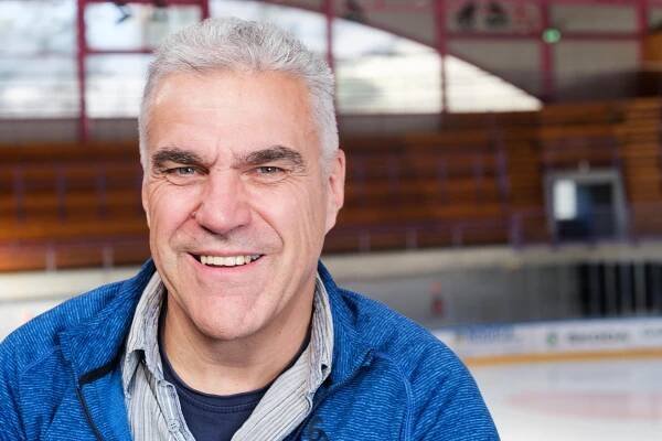 Jörg Eberle lächelt Richtung Kamera mit einer blauen Jacke in einer Eishalle in Biasca.