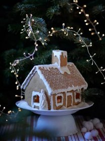 Mini perníková chaloupka VINTERSAGA je ozdobená polevou na stojanu před vánočním stromem.