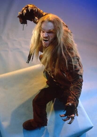 Person in werewolf costume with long hair and claws, posing on a platform, showing a dramatic expression