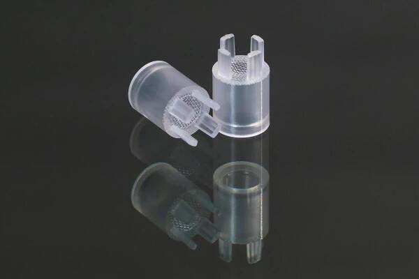 Two small, transparent, cylindrical plastic pieces with prongs and textured handles are depicted on a dark, reflective surface, with one lying on its side and the other standing upright.