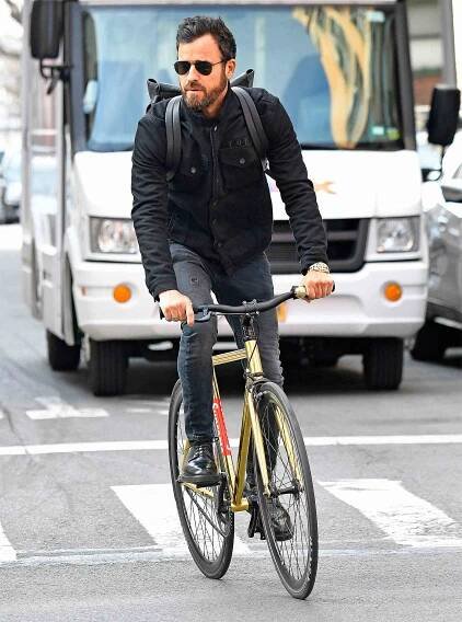 Justin Theroux rides his bike wearing gold bling to match his golden bike with a dark jacket and dark pants in New York City