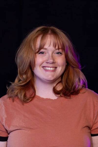 A woman with red hair is smiling for the camera in front of a black background.