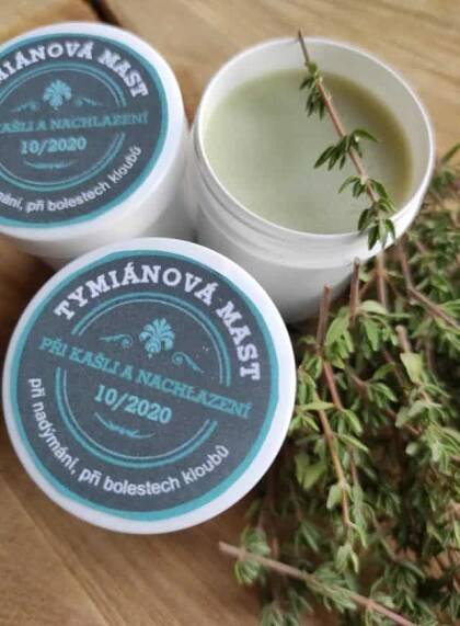 three small containers of wax sitting on top of a wooden table next to some plants