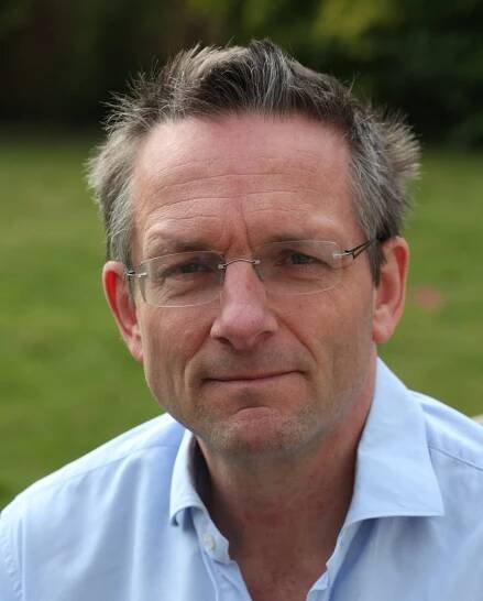 A close-up portrait of Michael Mosley wearing glasses and a light blue dress shirt.