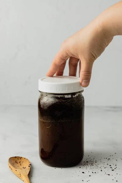 A hand puts a white lids on a large jar of homemade cold brew.