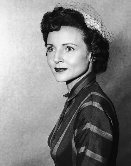 A person in vintage attire with a lace hat, looking past the camera