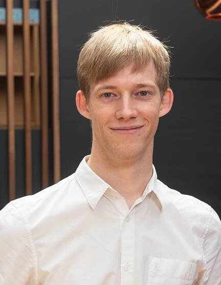 A white man with light brown hair, wearing a white shirt.