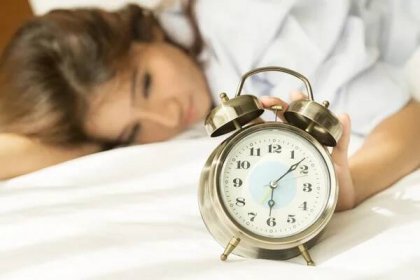Mladá asijská žena v posteli snaží probudit s budíkem — Stock fotografie