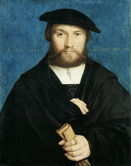 A pale man with a mustache and beard faces the viewer, wrapped in a black cloak and clutching a pair of gloves