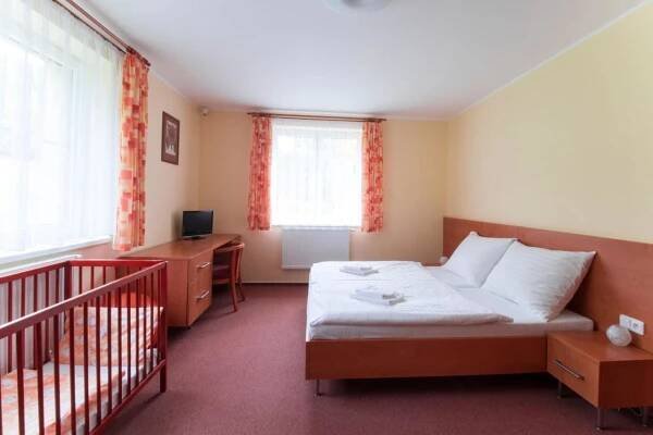 a bedroom with a bed and a desk and a crib at Hotel České Žleby in Stožec