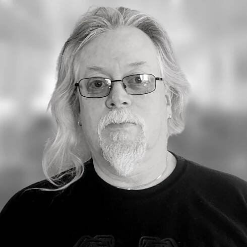 Man with long gray hair, goatee, and glasses. Wearing a black shirt.