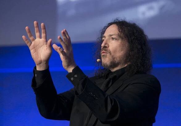 photo of David Berman wearing a microphone, speaking on stage with hands in air