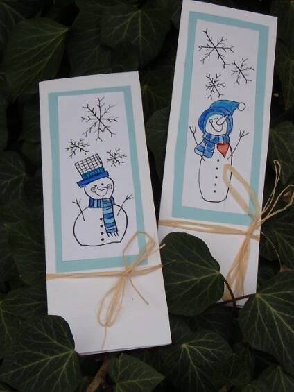 two cards with snowmen drawn on them are tied to green leaves and have brown twine