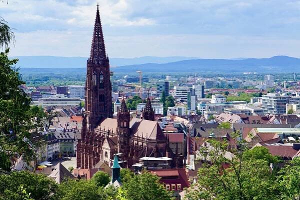 View of Freiburg with red church, square and lots of trees with the mountains behind
