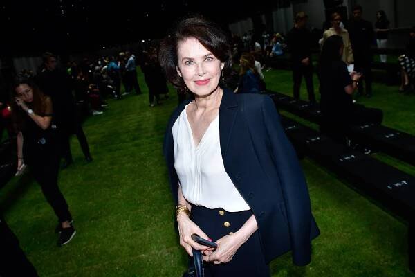 A woman with a blue jacket and white blouse smiles for the camera during a fashion event.