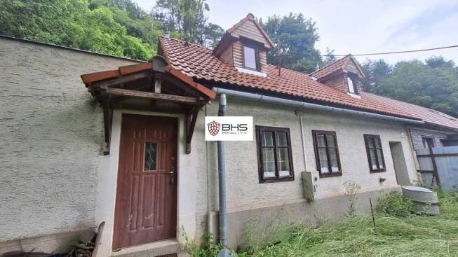 Rodinný dům v Perneku s tradiční střechou a dřevěnými okny, obklopený zelení.