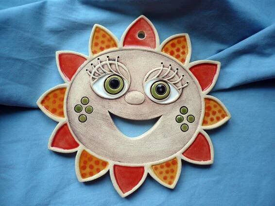 a ceramic sunflower with eyes on it's face is hanging from a blue cloth