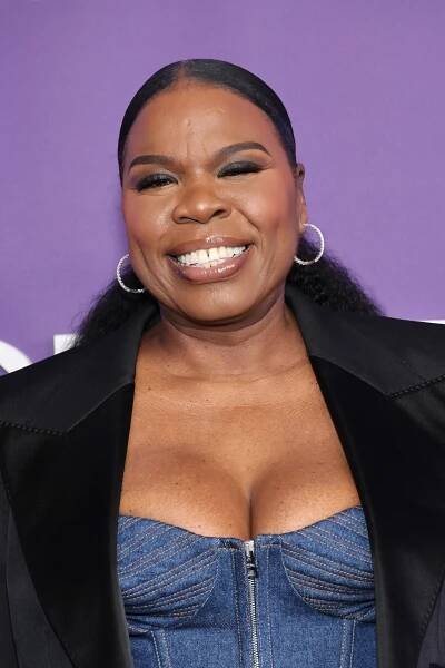 Leslie Jones smiling on a red carpet, wearing a denim bustier top under a tailored black blazer