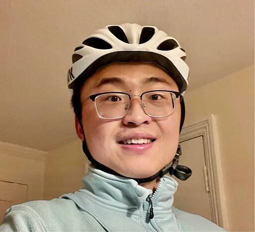 A heads hot of Harvard math graduate student Franklin Shiyi Wang wearing a white bike helmet, a light blue zip-up hoodie, and glasses.