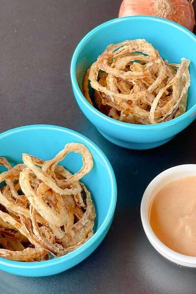 Crispy fried onion rings in 2 round blue ceramic bowls and a dip in a white small round bowl on the bottom right corner.