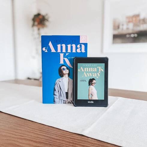 book anna k and kindle anna k away on wood table with white table runner. plant hanging in background