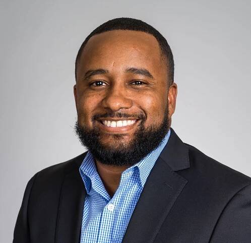 A man with a beard is wearing a suit and smiling for the camera.