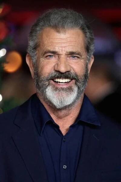 a close up of a person wearing a suit and smiling at the camera with a christmas tree in the background