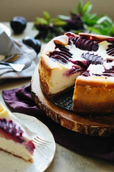 Plum ricotta cheesecake with a slice missing, sitting on a wood board.