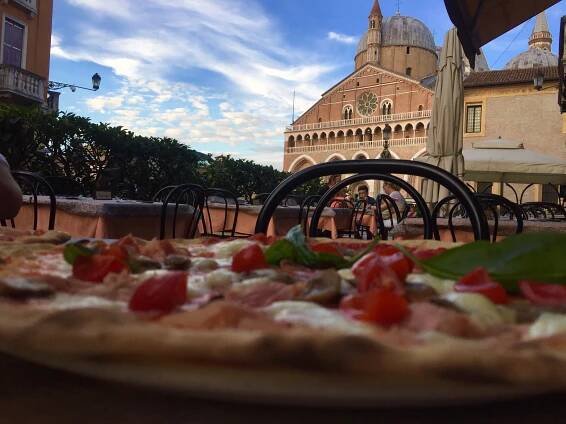 a pizza sitting on top of a pan covered in cheese and toppings next to a building
