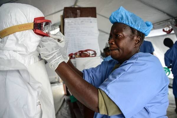  A nurse at an ETU in Kenema, Sierra Leone oversees a physician as she puts on the Personal Protective Equipment (PPE) before entering the 'Red Zone' of the ETU. October 2014 