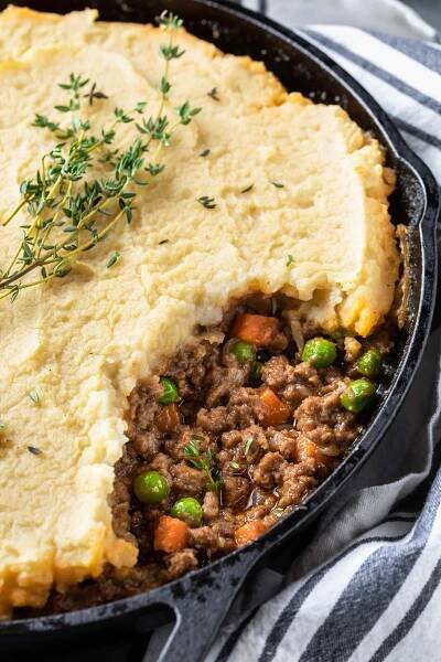 a close up of a cast iron dish of garnished shepherds pie missing a scoop