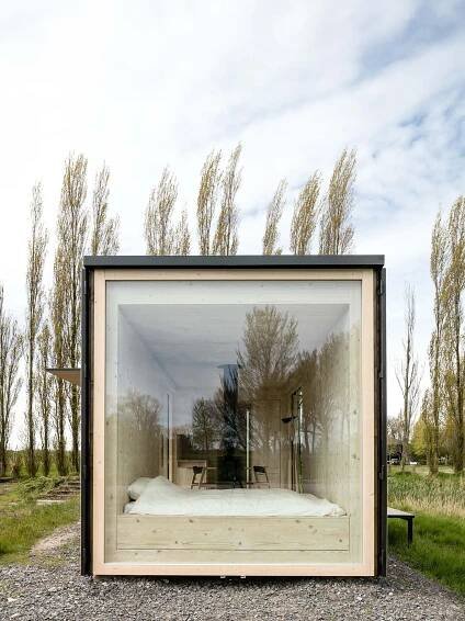 a bed sitting inside of a glass box on top of a gravel field next to trees