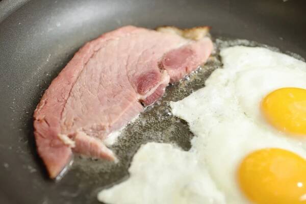 Slice of Wild Fork Bone-In Berkshire Smoked Ham being fried in a pan with two eggs