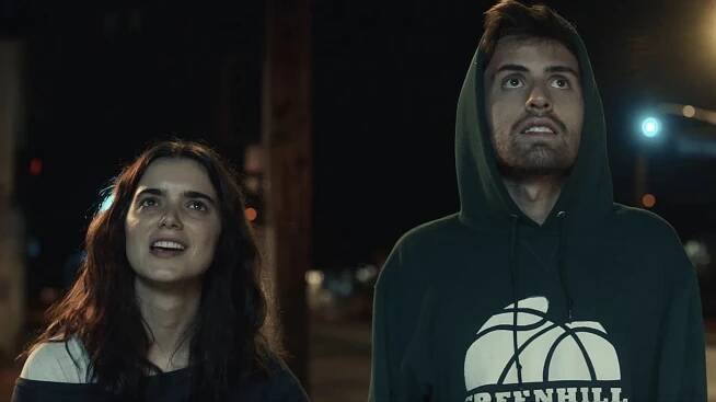 A boy and girl stand next to each other, look up, and stare.