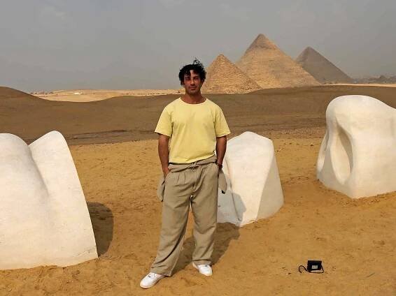 Jwan Yosef poses next to his sculpture "Vital Sands" at the Giza pyramids necropolis during the second edition of the Art D’Égypte exhibition "Forever is Now" on October 27, 2022 in Giza, Egypt