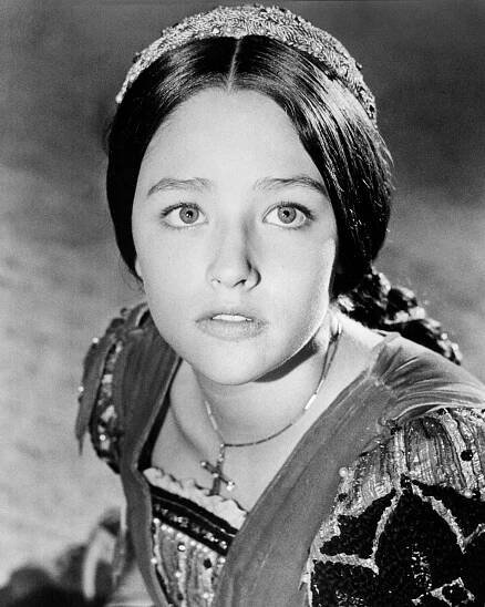 A young girl in a period costume stares up at the camera.