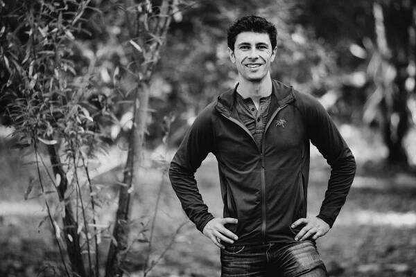 Black and white portrait of someone in casual attire standing outdoors among trees.